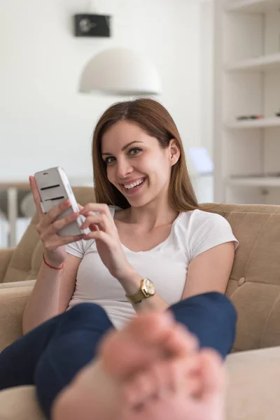 Mulher sentada no sofá com telefone celular — Fotografia de Stock