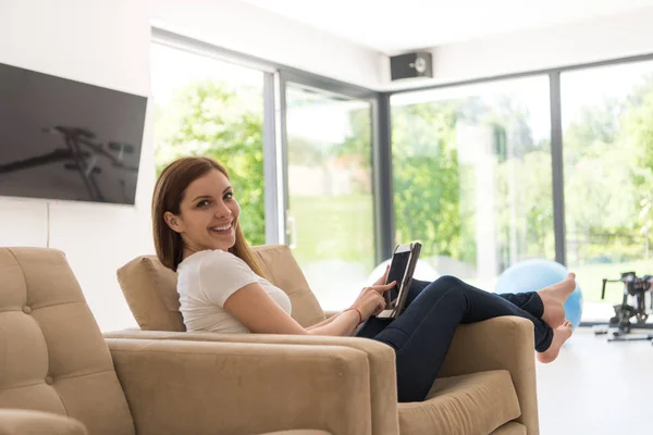Жінка сидить на дивані з планшетним комп'ютером — стокове фото