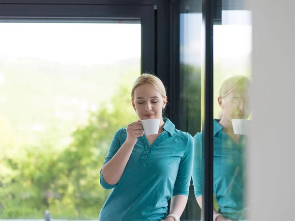 Młoda kobieta picia porannej kawy przez okno — Zdjęcie stockowe