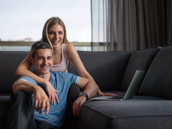 Casal atraente usando um laptop no sofá — Fotografia de Stock