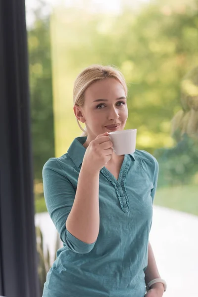 Ung kvinna dricka morgonkaffe vid fönstret — Stockfoto