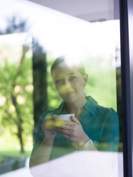 Młoda kobieta picia porannej kawy przez okno — Zdjęcie stockowe