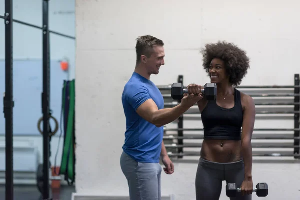 Černá žena dělá bicep kroutí s fitness trenérem — Stock fotografie
