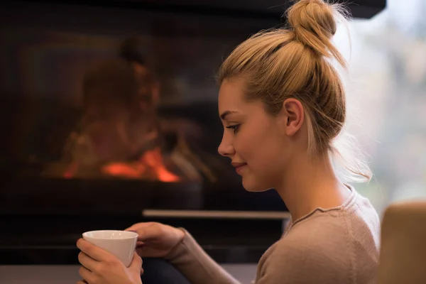 Молода жінка п'є каву перед каміном — стокове фото