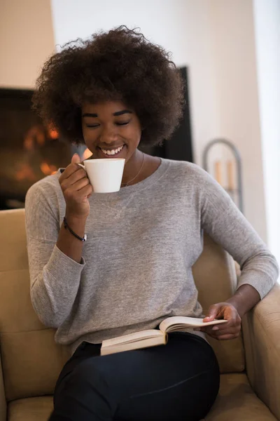Чернокожая женщина читает книгу перед камином — стоковое фото
