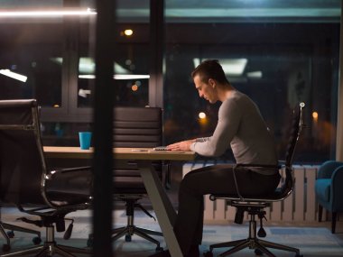 karanlık ofiste dizüstü bilgisayarda çalışan adam