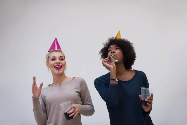 Mulheres sorridentes em bonés de festa soprando para assobios — Fotografia de Stock