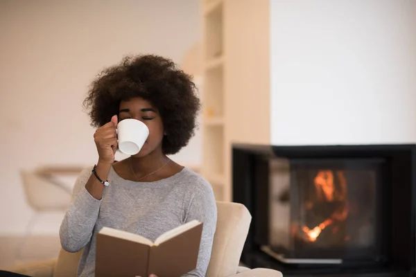 Чернокожая женщина читает книгу перед камином — стоковое фото
