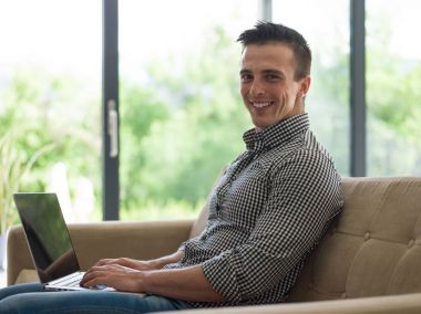 Oturma odasında dizüstü bilgisayar kullanan adam.