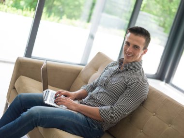 Oturma odasında dizüstü bilgisayar kullanan adam.