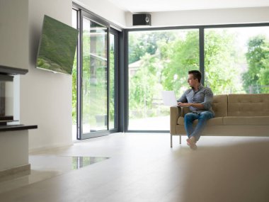 Oturma odasında dizüstü bilgisayar kullanan adam.