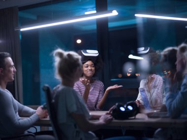 Gece ofisinde sanal gerçeklik kulaklığı kullanan çok ırklı iş adamları yaratıcı ofisteki masanın etrafında sanal gerçeklik simülatörüyle buluşuyor..