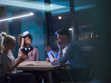Gece ofisinde sanal gerçeklik kulaklığı kullanan çok ırklı iş adamları yaratıcı ofisteki masanın etrafında sanal gerçeklik simülatörüyle buluşuyor..