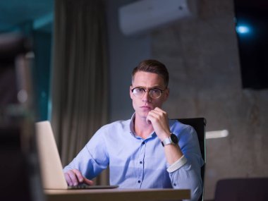 karanlık ofiste dizüstü bilgisayarda çalışan adam