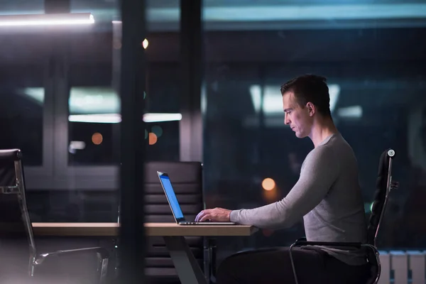 Uomo che lavora su computer portatile in ufficio scuro — Foto Stock