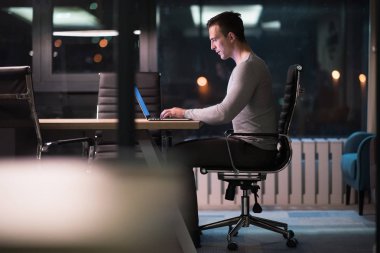 karanlık ofiste dizüstü bilgisayarda çalışan adam