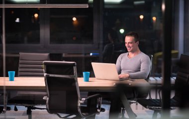 karanlık ofiste dizüstü bilgisayarda çalışan adam