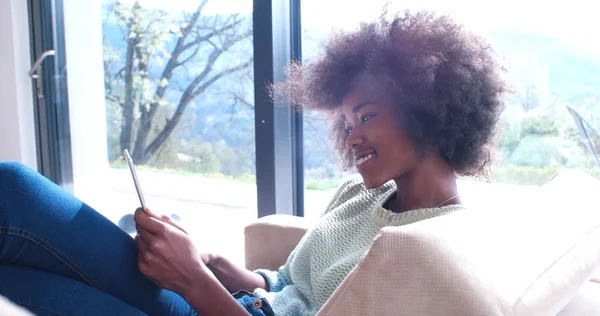 Чорна жінка сидить на дивані і використовує мобільний телефон — стокове фото