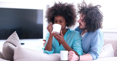 çok ırklı çift evde kanepede oturmuş kahve içme