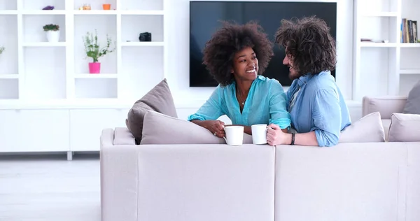 Pareja multiétnica sentada en el sofá en casa bebiendo café —  Fotos de Stock