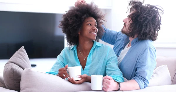 Multiethnisches Paar sitzt zu Hause auf Sofa und trinkt Kaffee — Stockfoto