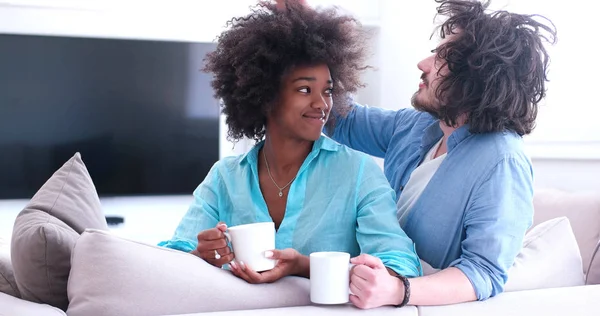 Multiethnisches Paar sitzt zu Hause auf Sofa und trinkt Kaffee — Stockfoto