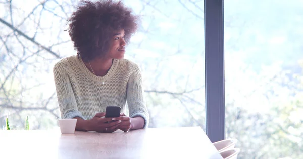 Mujer negra bebiendo café y usando un teléfono móvil en casa —  Fotos de Stock
