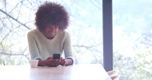 Mujer negra bebiendo café y usando un teléfono móvil en casa —  Fotos de Stock