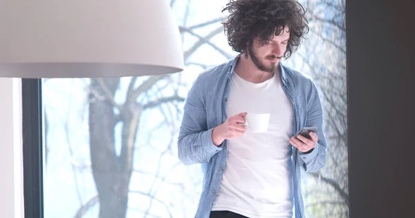 Joven bebiendo café y usando un teléfono móvil en casa — Foto de Stock