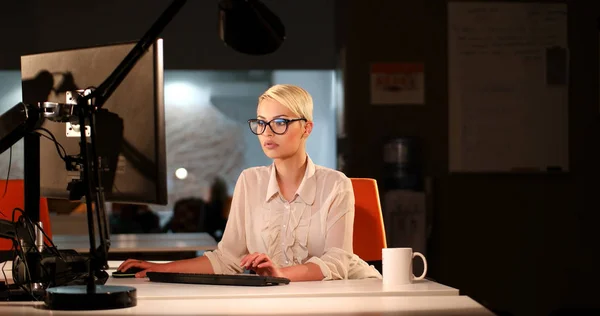 Жінка працює на комп'ютері в темному офісі — стокове фото