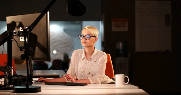 Жінка працює на комп'ютері в темному офісі — стокове фото