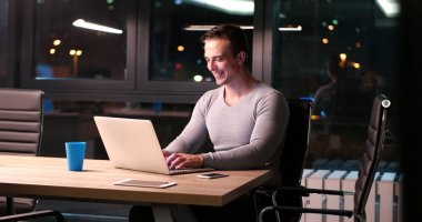 karanlık ofiste dizüstü bilgisayarda çalışan adam