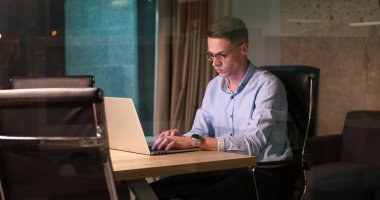 karanlık ofiste dizüstü bilgisayarda çalışan adam