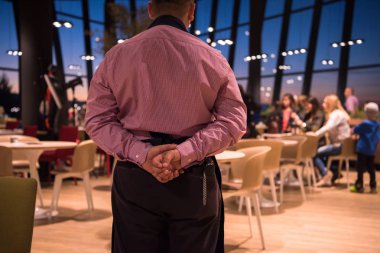 Lüks bir restoranda elleri arkada duran kendine güvenen genç bir garsonun arka manzarası.