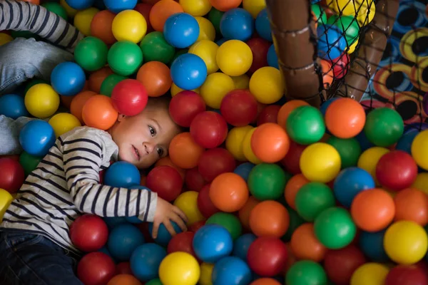 Мальчик веселится в сотнях разноцветных пластиковых шаров — стоковое фото