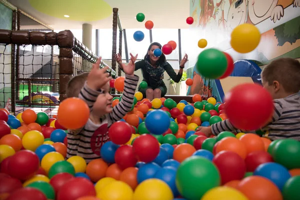 Jovem mãe com seus filhos em uma sala de jogos infantil — Fotografia de Stock