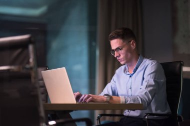 karanlık ofiste dizüstü bilgisayarda çalışan adam