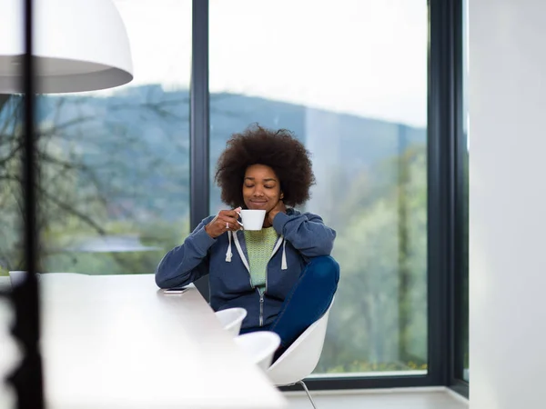 Svart kvinna dricka kaffe och använder en mobiltelefon hemma — Stockfoto
