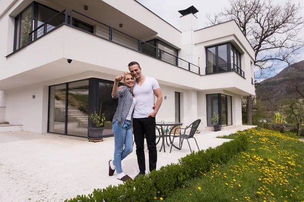 Pareja abrazándose frente a una nueva casa de lujo — Foto de Stock