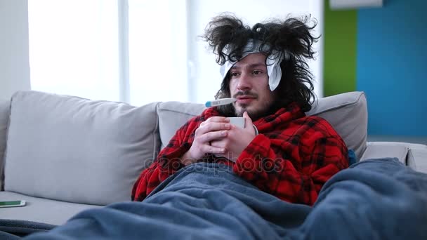 Chory człowiek trzyma kubek siedząc na kanapie — Wideo stockowe