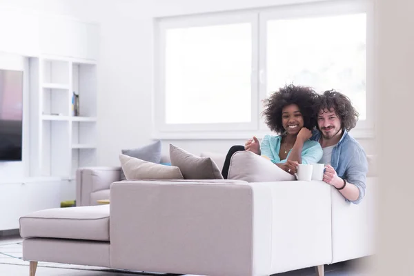 Pareja multiétnica sentada en el sofá en casa bebiendo café —  Fotos de Stock