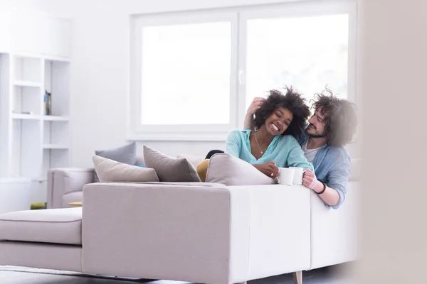 多民族のカップルが自宅のソファに座ってコーヒーを飲んでください。 — ストック写真
