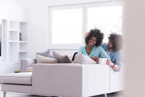 Multietniskt paret sitter på soffan hemma dricker kaffe — Stockfoto