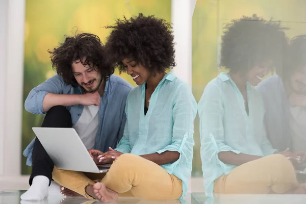Casal multiétnico usando um laptop no chão — Fotografia de Stock