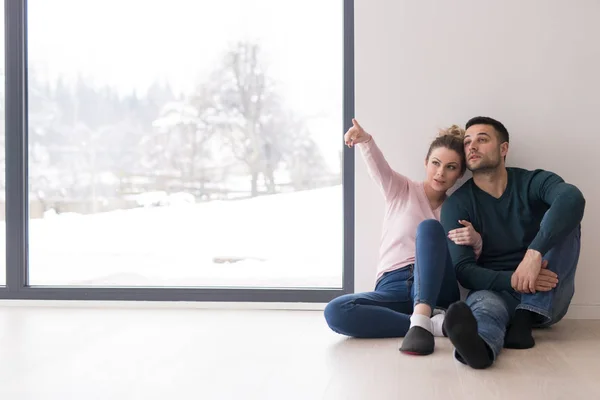 Молода пара сидить на підлозі біля вікна вдома — стокове фото