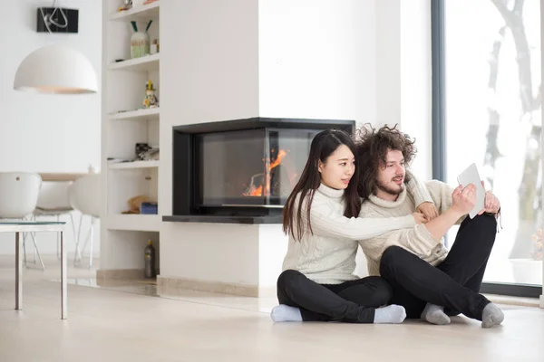 Multiethnisches Paar mit Tablet-Computer vor dem Kamin — Stockfoto