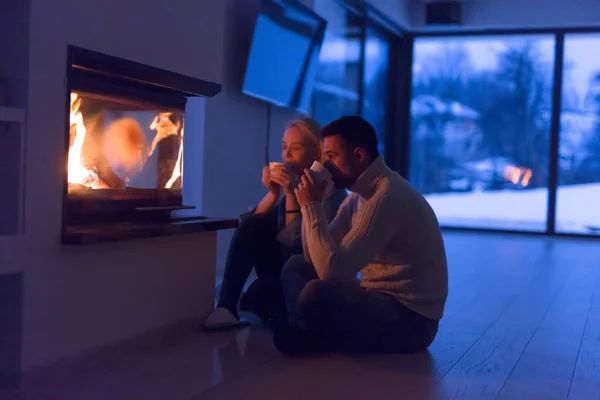 Junges romantisches Paar sitzt gemütlich vor dem heimischen Kamin