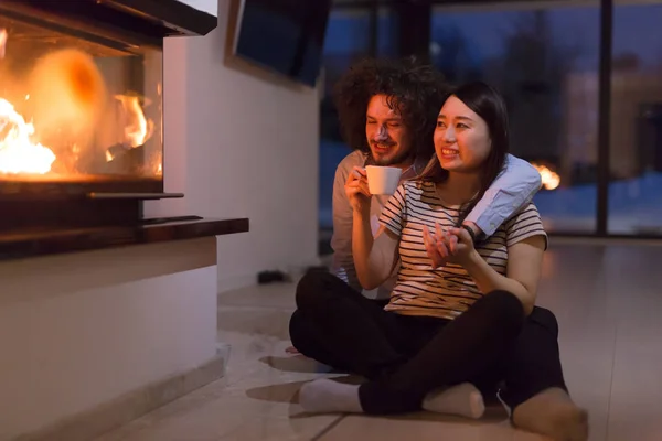 Feliz casal multiétnico sentado na frente da lareira — Fotografia de Stock