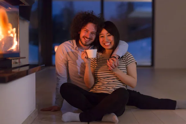 Feliz casal multiétnico sentado na frente da lareira — Fotografia de Stock