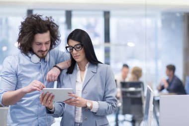 İş adamları, arka planda iş arkadaşlarıyla buluşmaya hazırlanırken tablet bilgisayarı kullanıyorlar ve başlangıç ofisinde fikirleri tartışıyorlar.